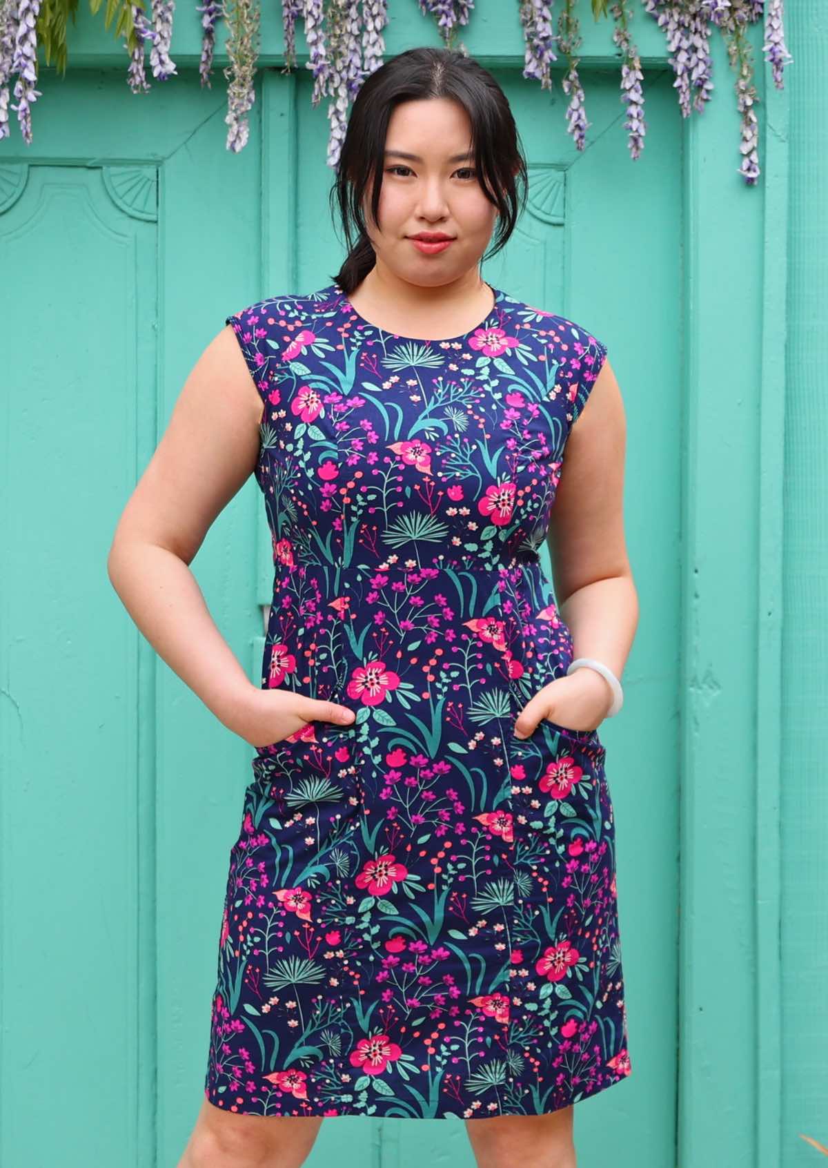 Woman with dark hair in 100% navy cotton floral dress with hands in pockets