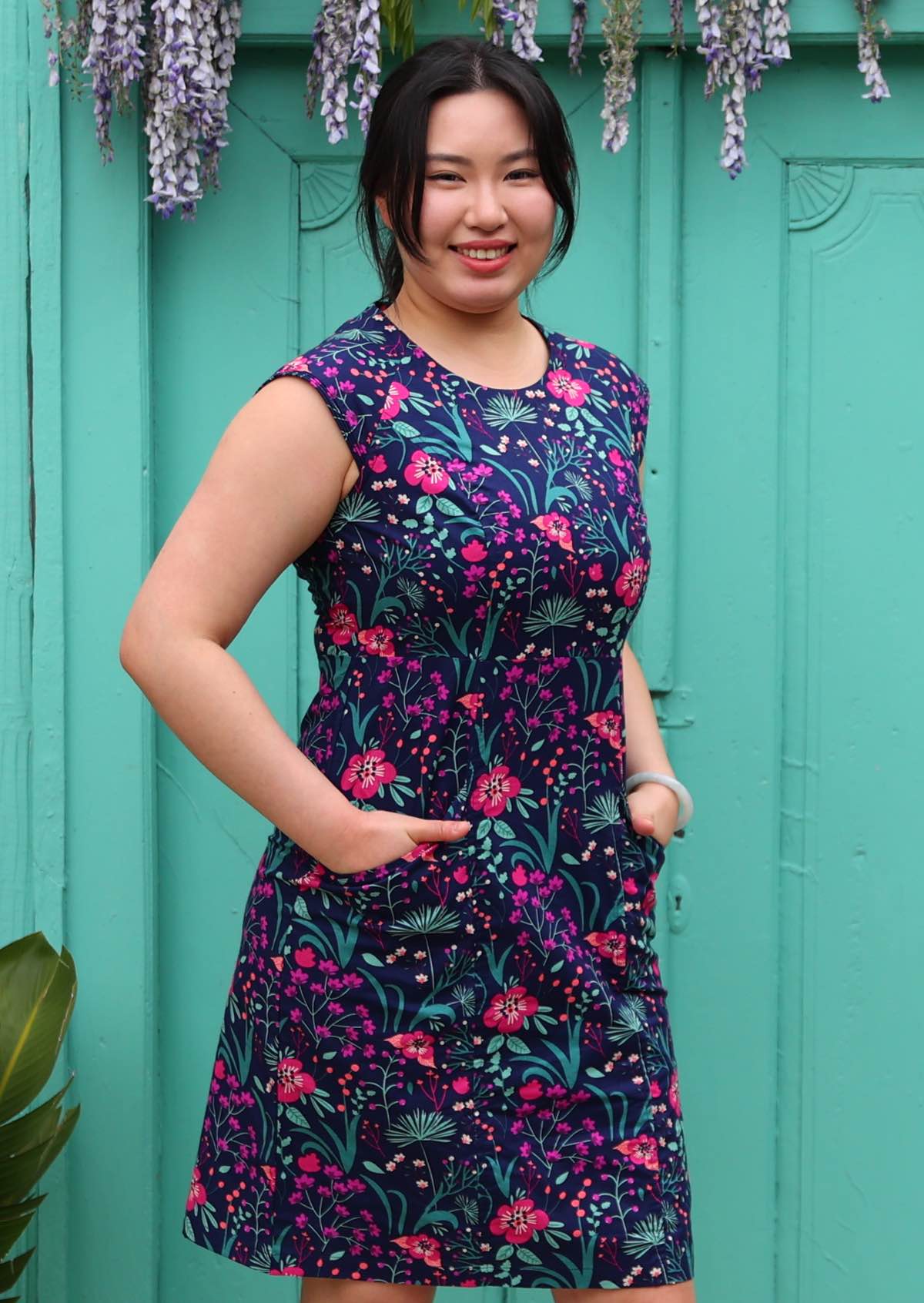 Woman with dark hair in 100% navy and purple cotton floral dress with hands in pockets