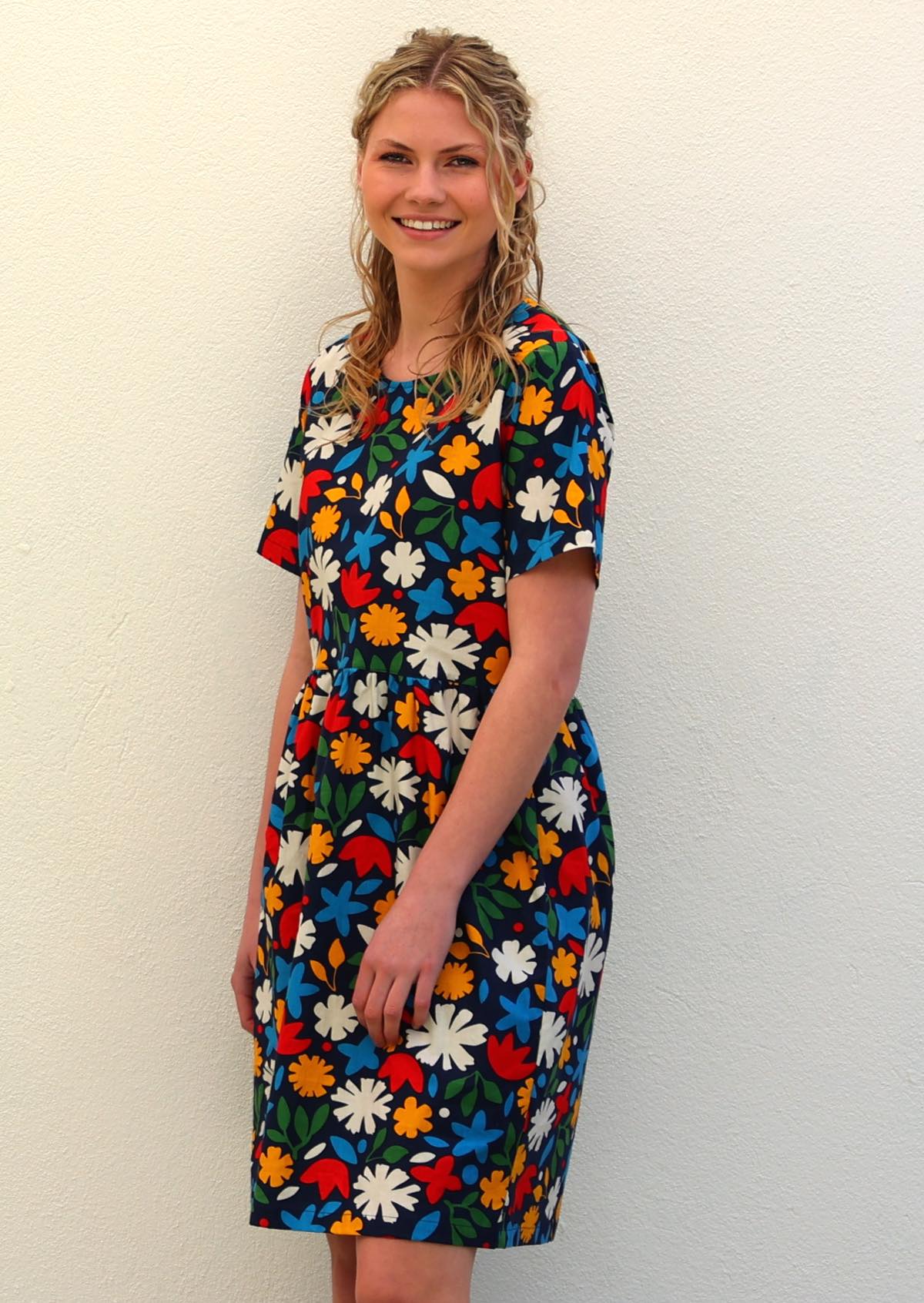 Model stands side on in cotton short sleeve above knee dress with round neckline, in retro abstract floral print