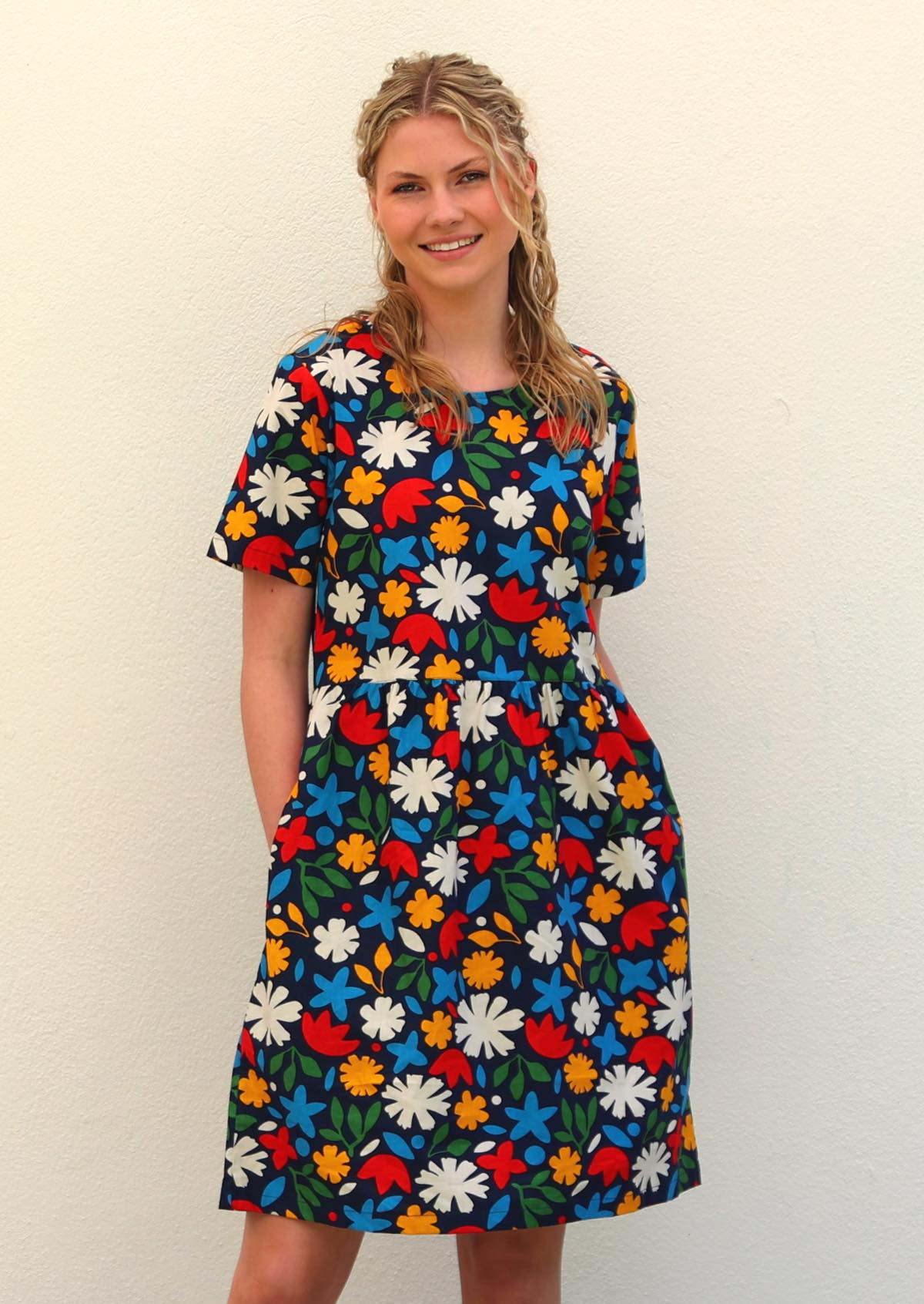 Model with blonde hair wearing 100 percent cotton dark navy blue base and bright abstract floral print cotton retro dress, with hands in deep pockets