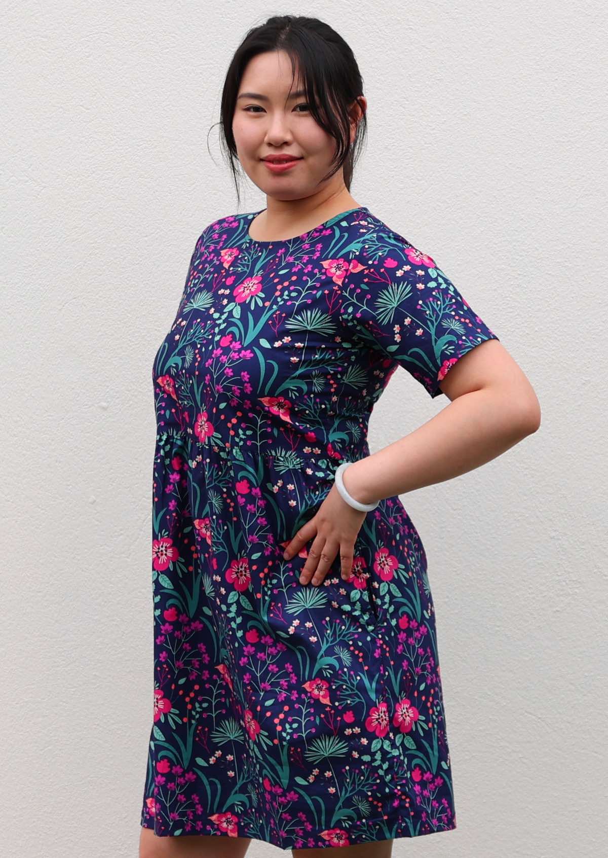 woman in loose fit purple, navy and pink floral print 100% cotton dress in front of white wall 