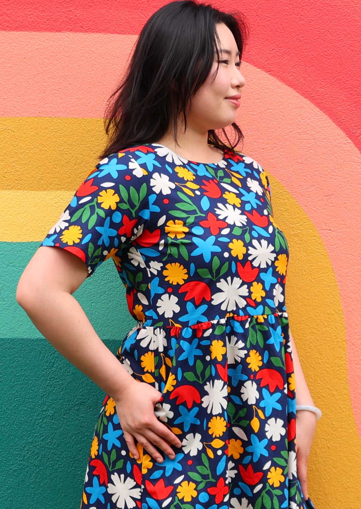 Close up of model in cotton dress with high round neckline and short sleeves, in bold floral print on dark blue base