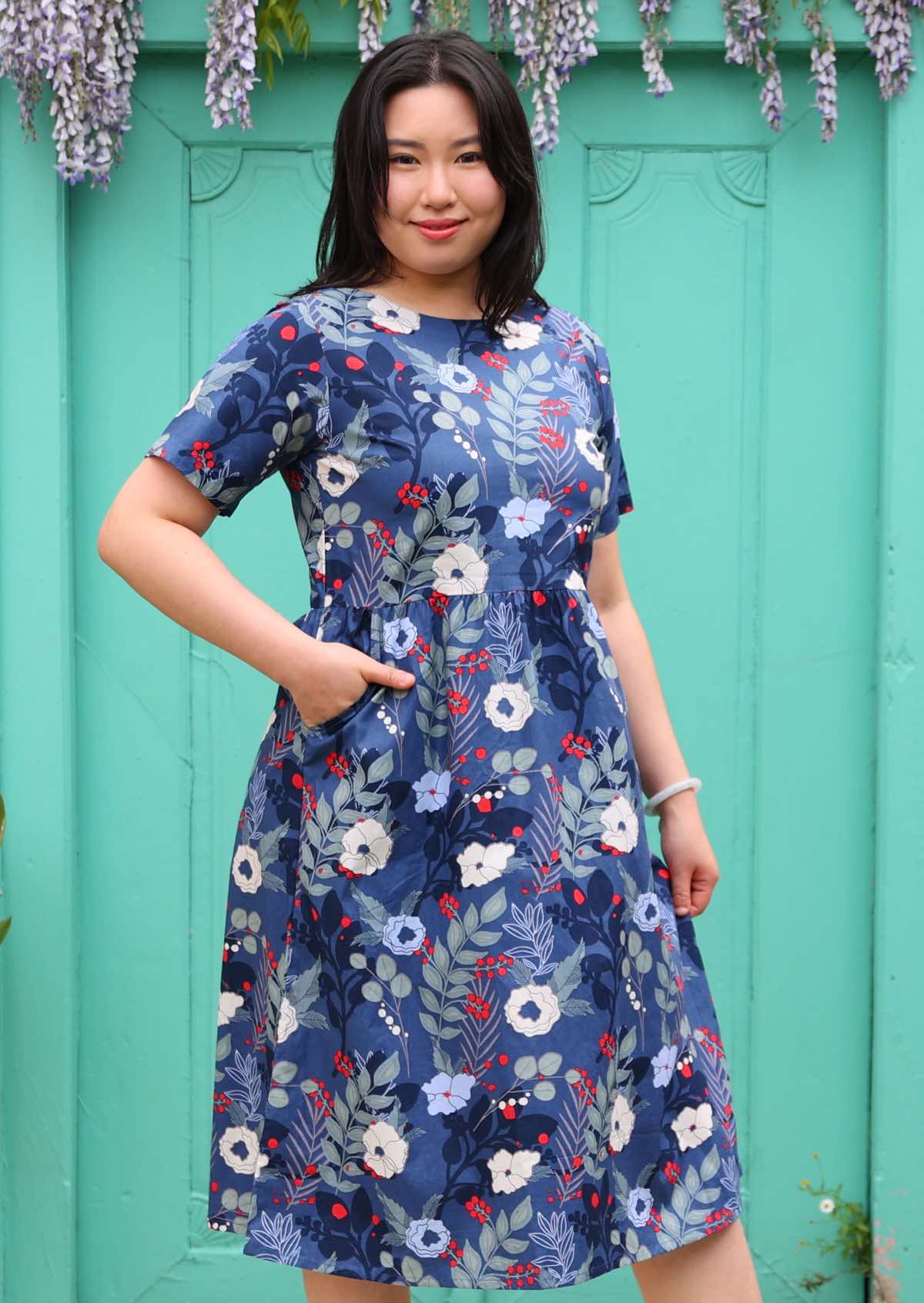 Model poses in blue floral print cotton midi length dress with high round neckline, t-shirt sleeves, with hand in side pocket