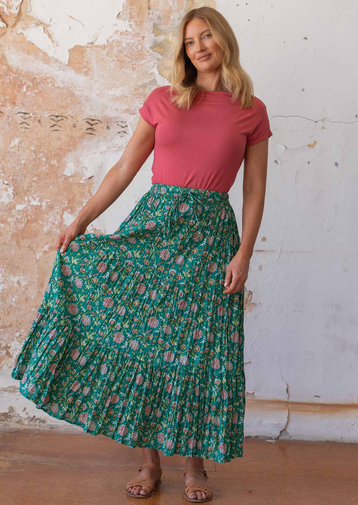 Model stands in three tiered cotton maxi skirt in floral print, holding the side out to display the volume of fabric