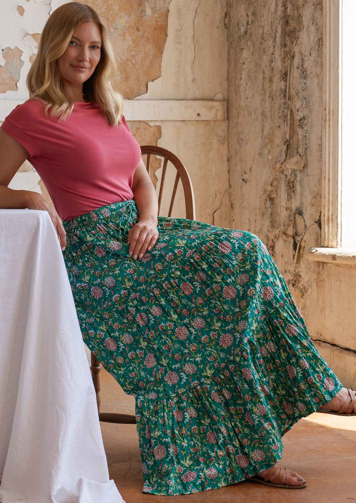 Model sitting in wooden chair wearing three tiered 100 percent cotton maxi skirt with elasticated waistband and drawstring