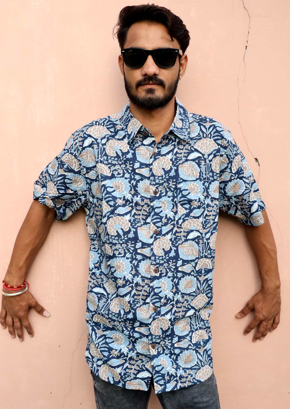 Man leaning against wall with blue floral print shirt in blue hues