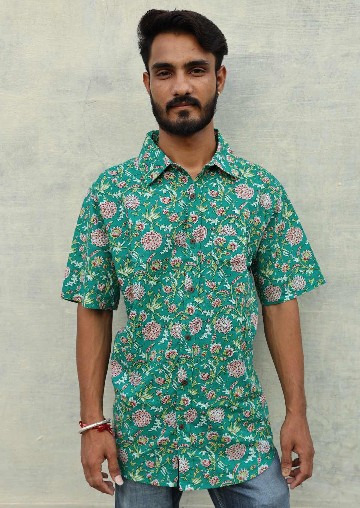 Man wears relaxed fit cotton short sleeve shirt with coconut button and one pocket on left side, in floral print on jade green base