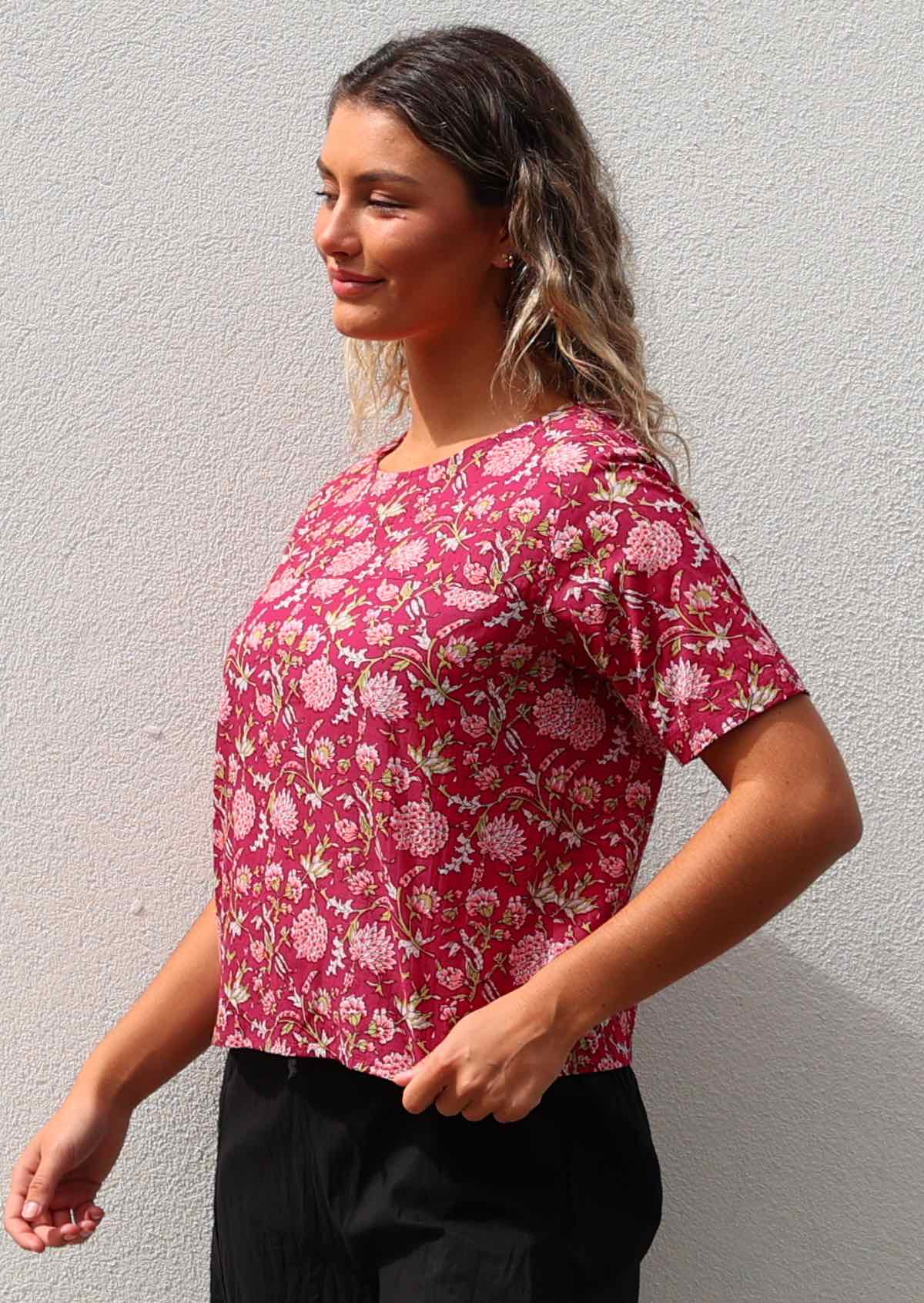 Woman stands sideways in 100% cotton floral print top with high round neckline and T-shirt sleeves