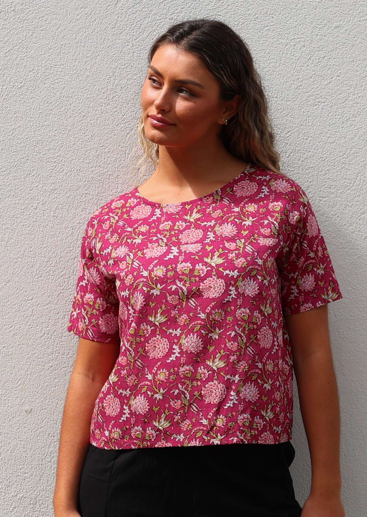 Woman wears cotton short sleeve relaxed fit top in floral print on a bright red base