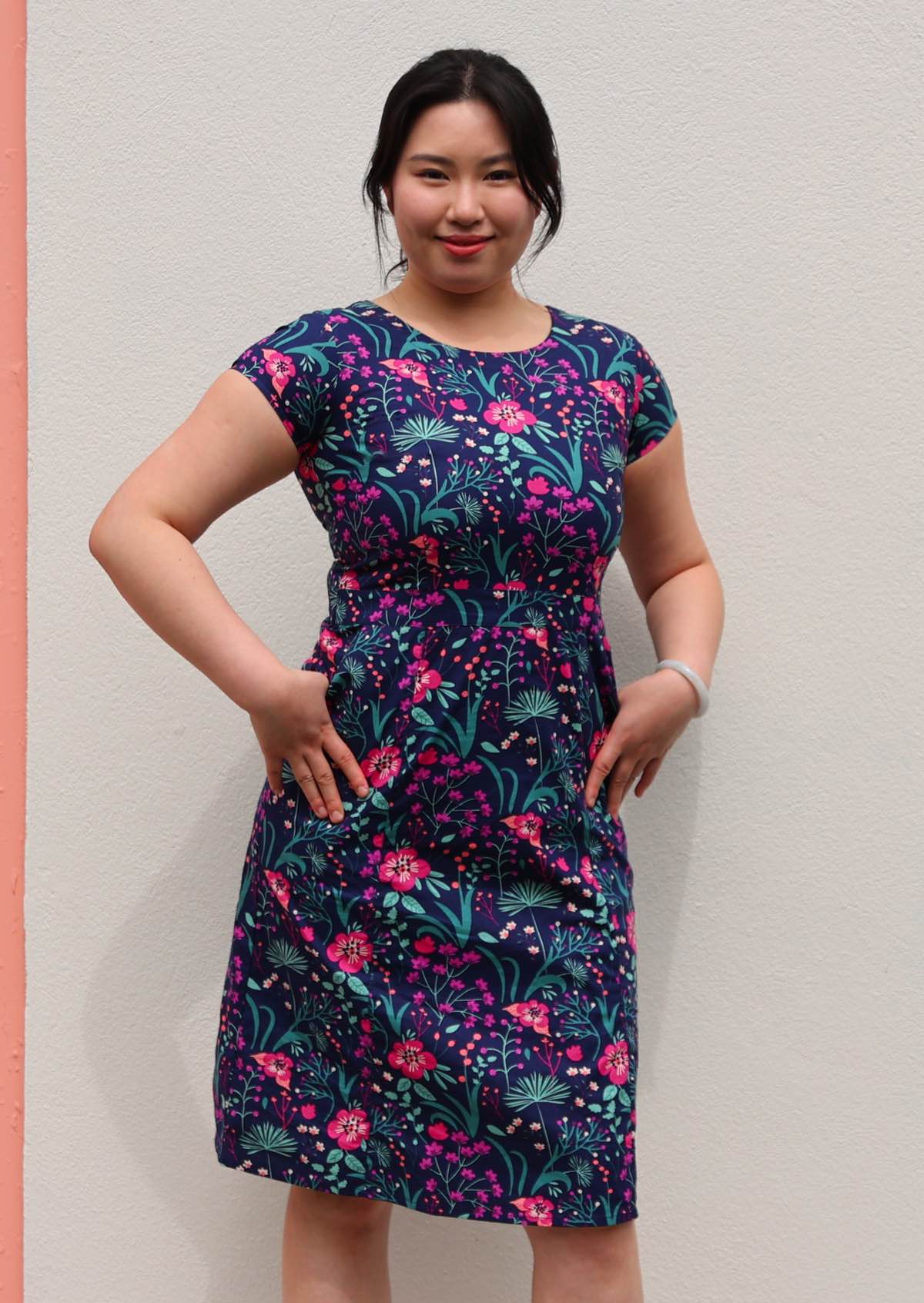 woman in navy and purple floral cotton knee length dress with round neckline and hands in pockets 