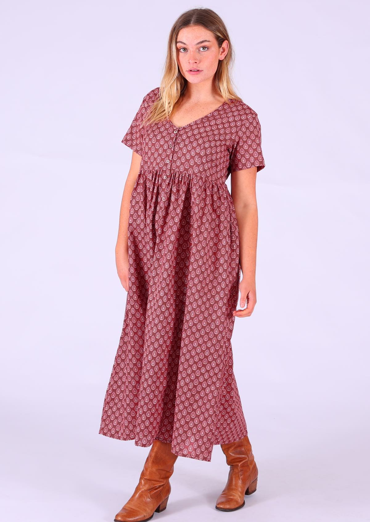 Model standing wearing 100 percent cotton dark terracotta maxi sundress v-neck with pockets paired with tan leather boots 