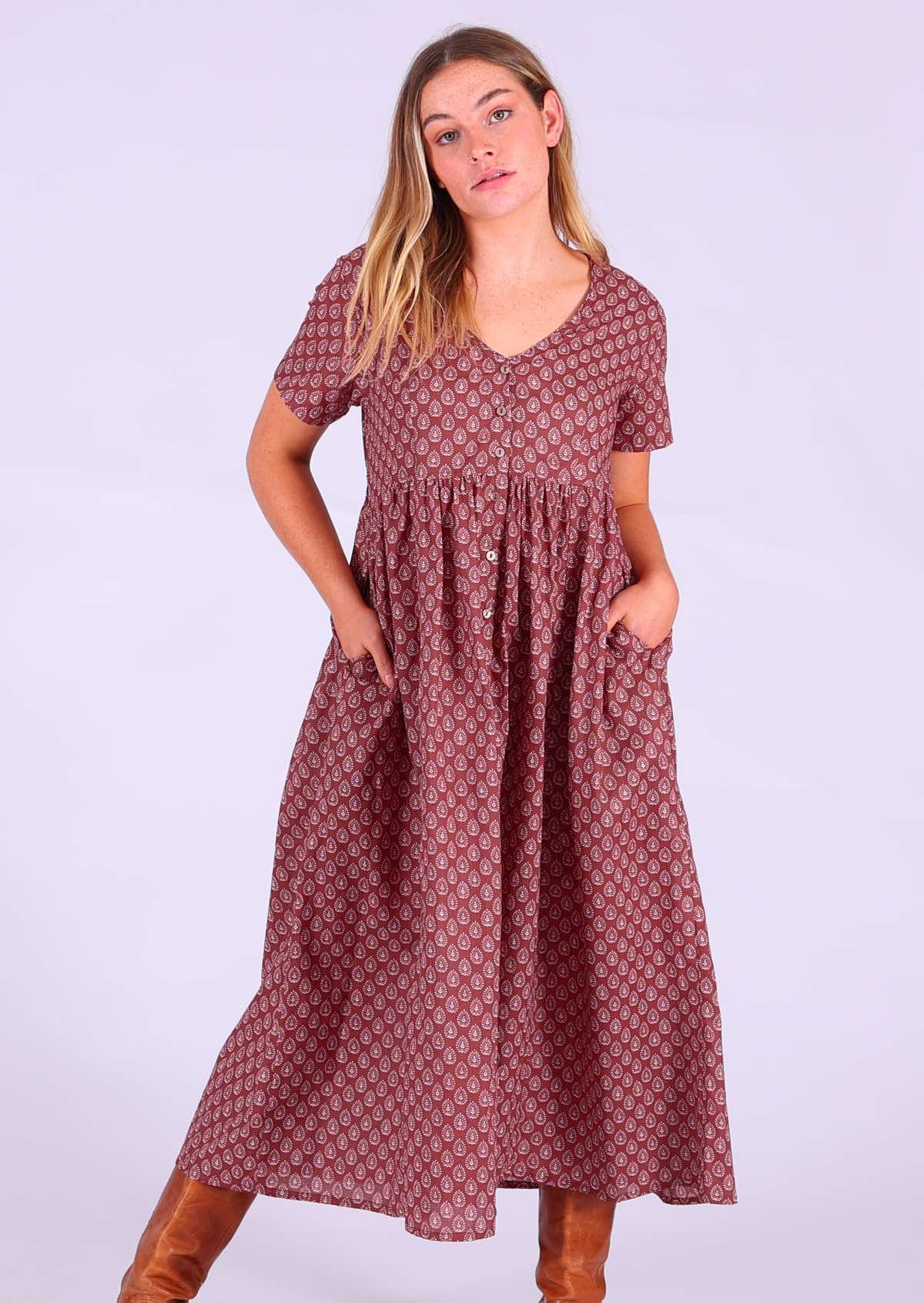 Model standing with hands in pockets wearing 100 percent cotton dark terracotta maxi sundress