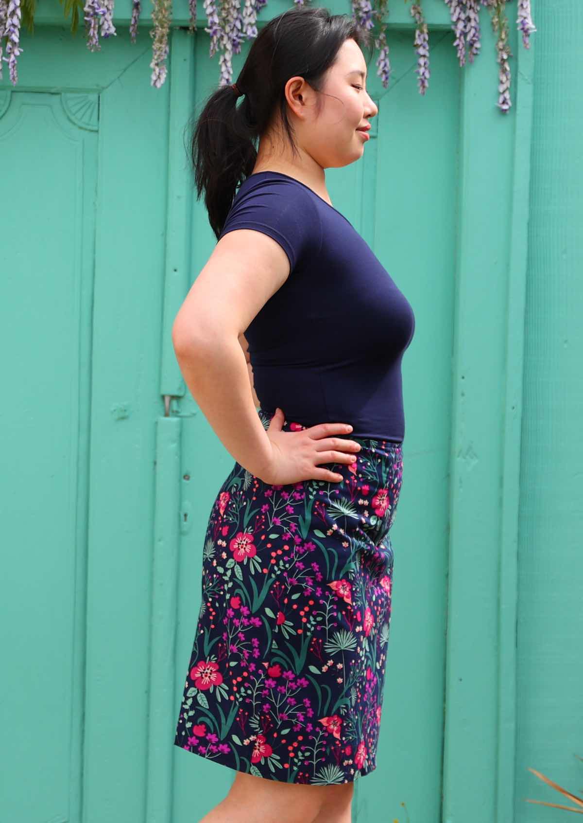 Side image of Model wearing purple floral print  reversible skirt 100 percent cotton knee length skirt with zip on the side.