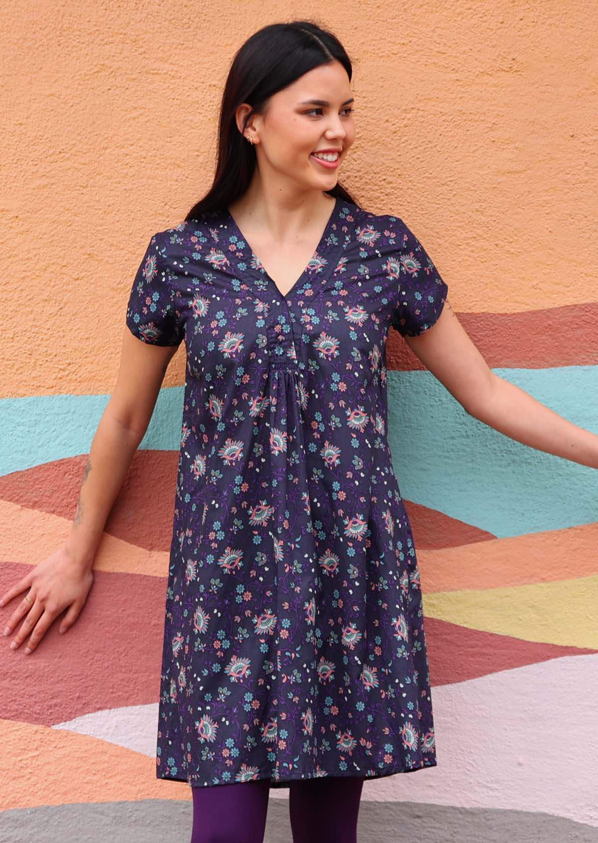 Model wearing short sleeve cotton dark purple tunic standing in front of wall 