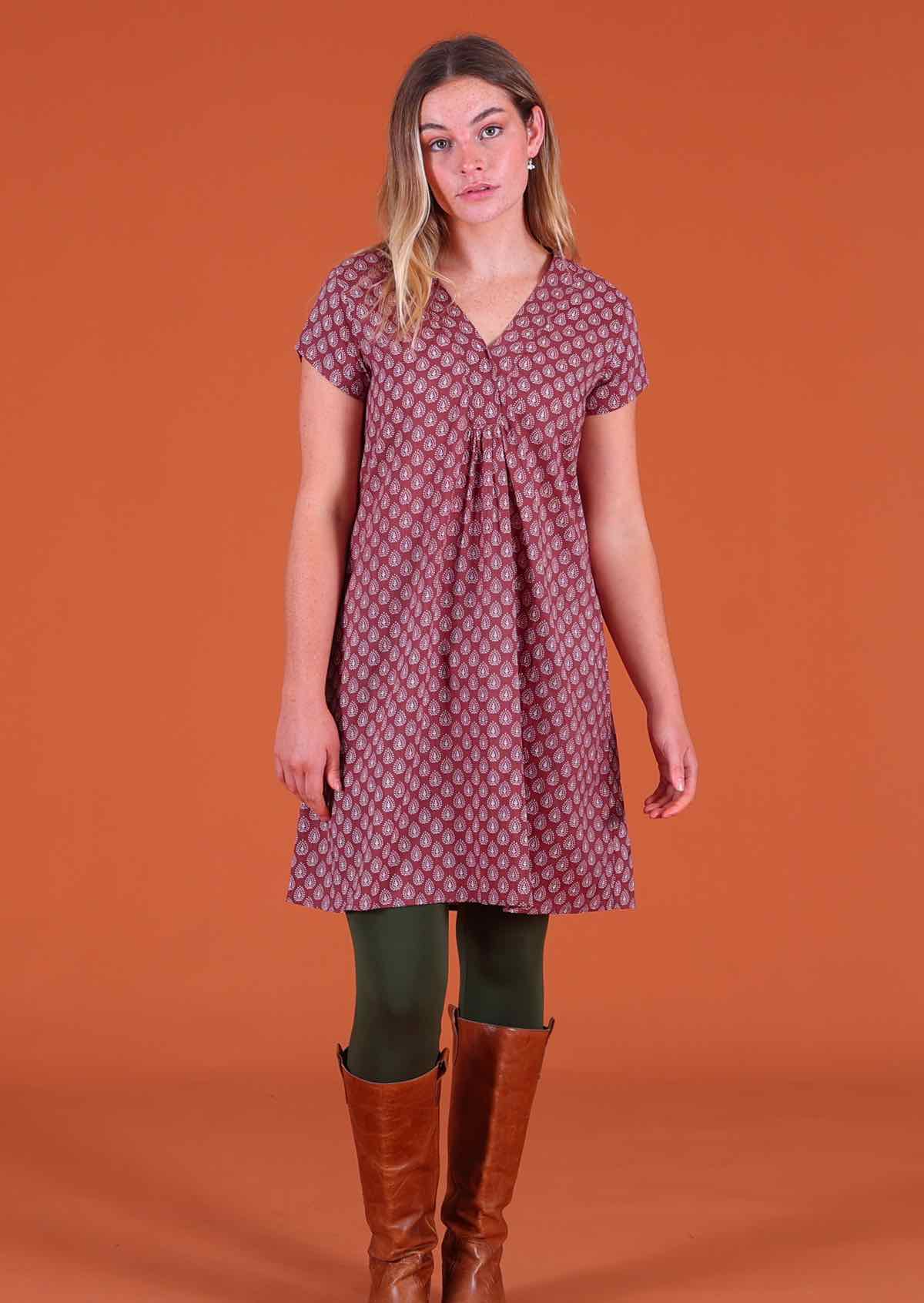 Woman standing, wearing the Sandy Tunic Henna 100 percent cotton white pendant block print on a dark terracotta base paired with tan boots 