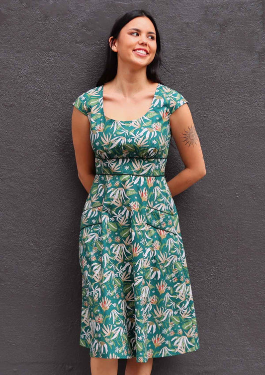 Model with green 100 percent cotton scoop neck retro dress with pockets standing against a wall 