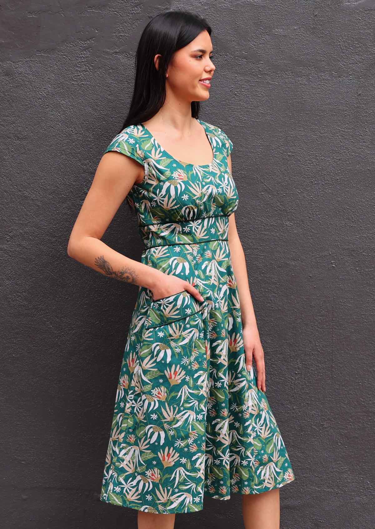 Model standing side on wearing green 100 percent cotton scoop neck retro dress with hand in pocket