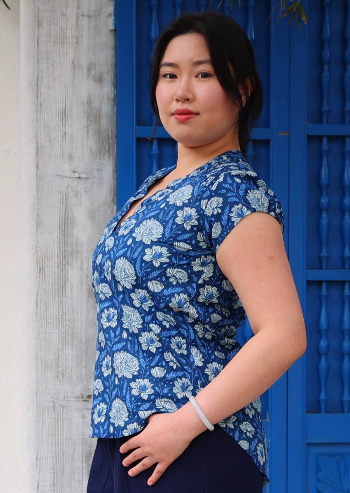 Model turned to the side wearing cotton blue floral top with cap sleeves, that is longer at the back