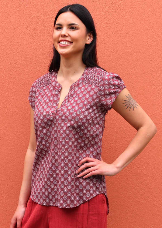 Model poses in dark terracotta cotton cap sleeve top with white pendant detail