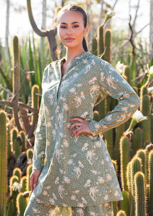 Model poses in long sleeve cotton tunic with V-neckline, buttons and a mandarin collar, in cream on pale green floral print