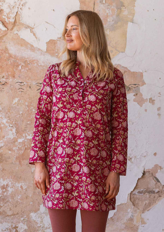 Woman stands in cotton V-neckline long sleeve tunic in a floral print with a bright red base