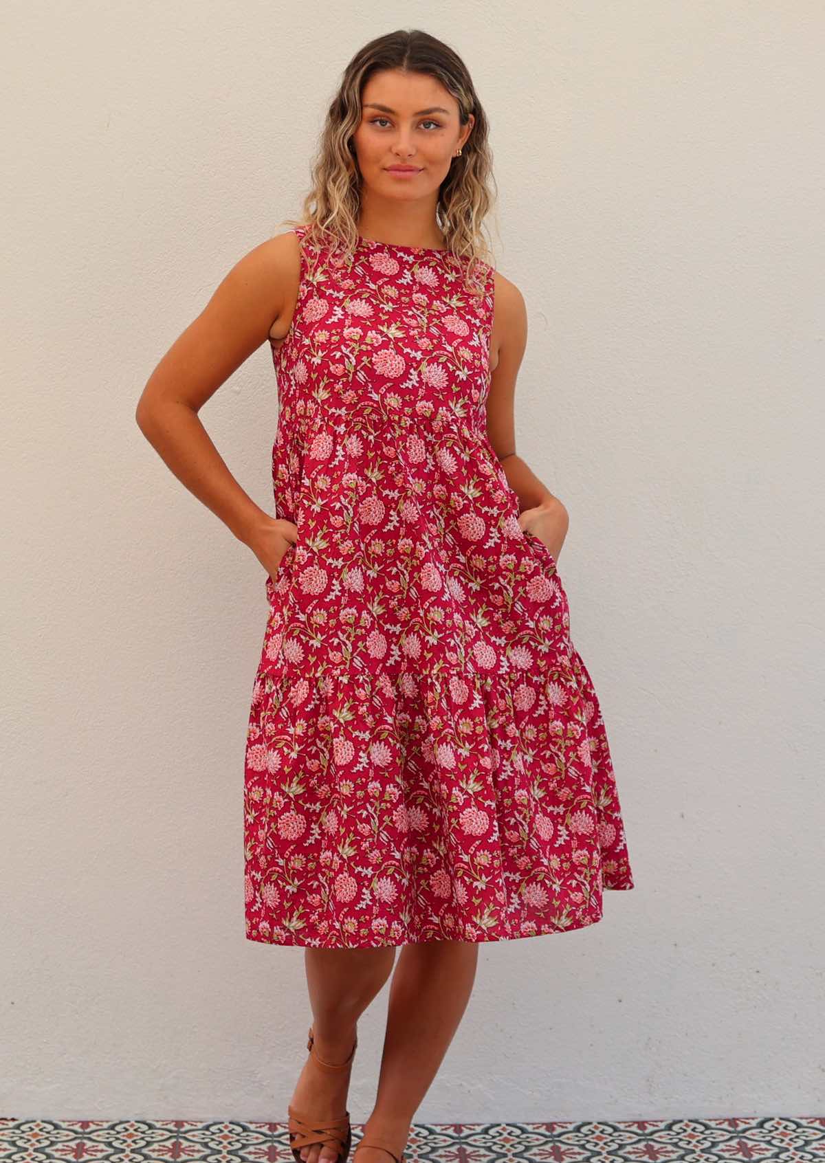 Woman wears cotton sleeveless three tiered midi length dress with hands in hidden side pockets