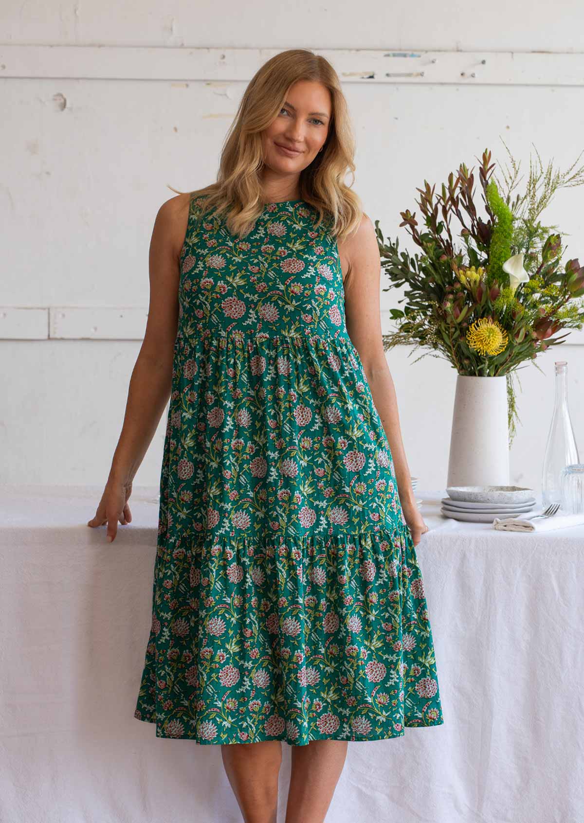 Woman wears cotton sleeveless three tiered midi length dress in floral print with jade green base