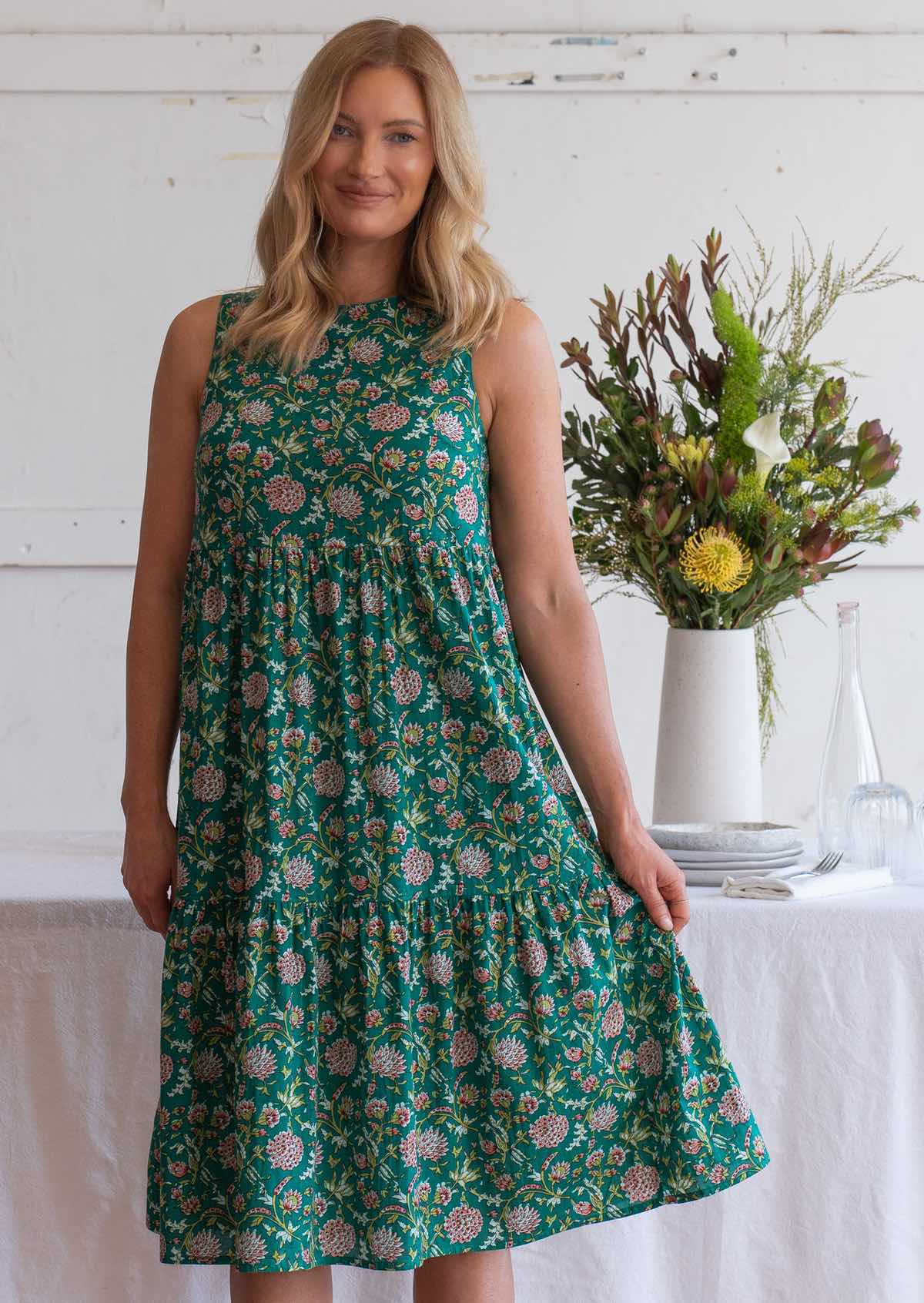 Model stands in floral print sleeveless three tiered midi length dress, holding side out to display volume of skirt