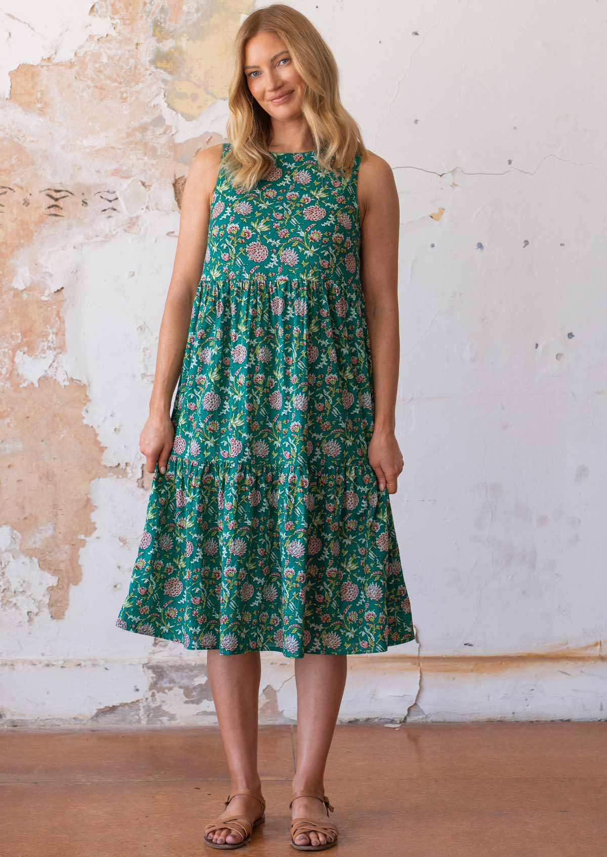 Model stands in cotton sleeveless midi length dress with high round neckline in floral print with a jade green base