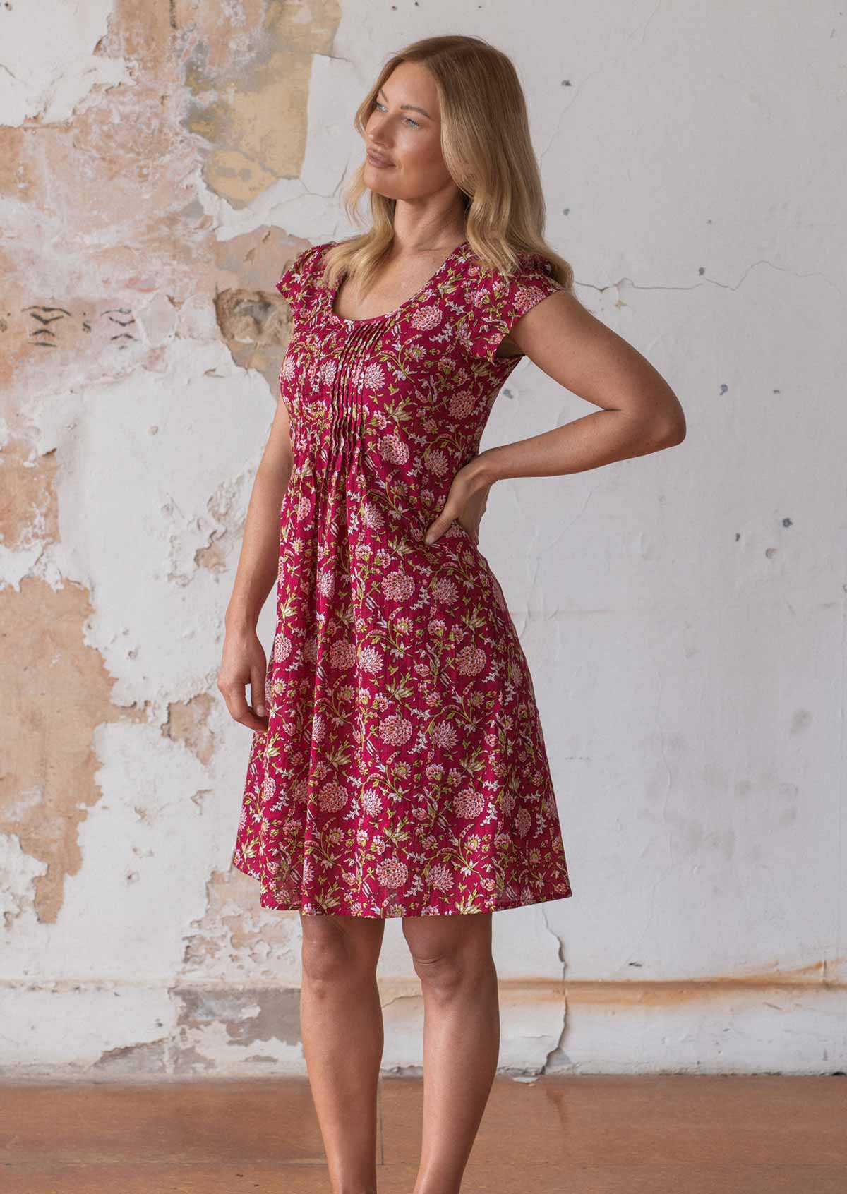 Woman stands with hand on hip in red based floral print cotton above knee dress with cap sleeves