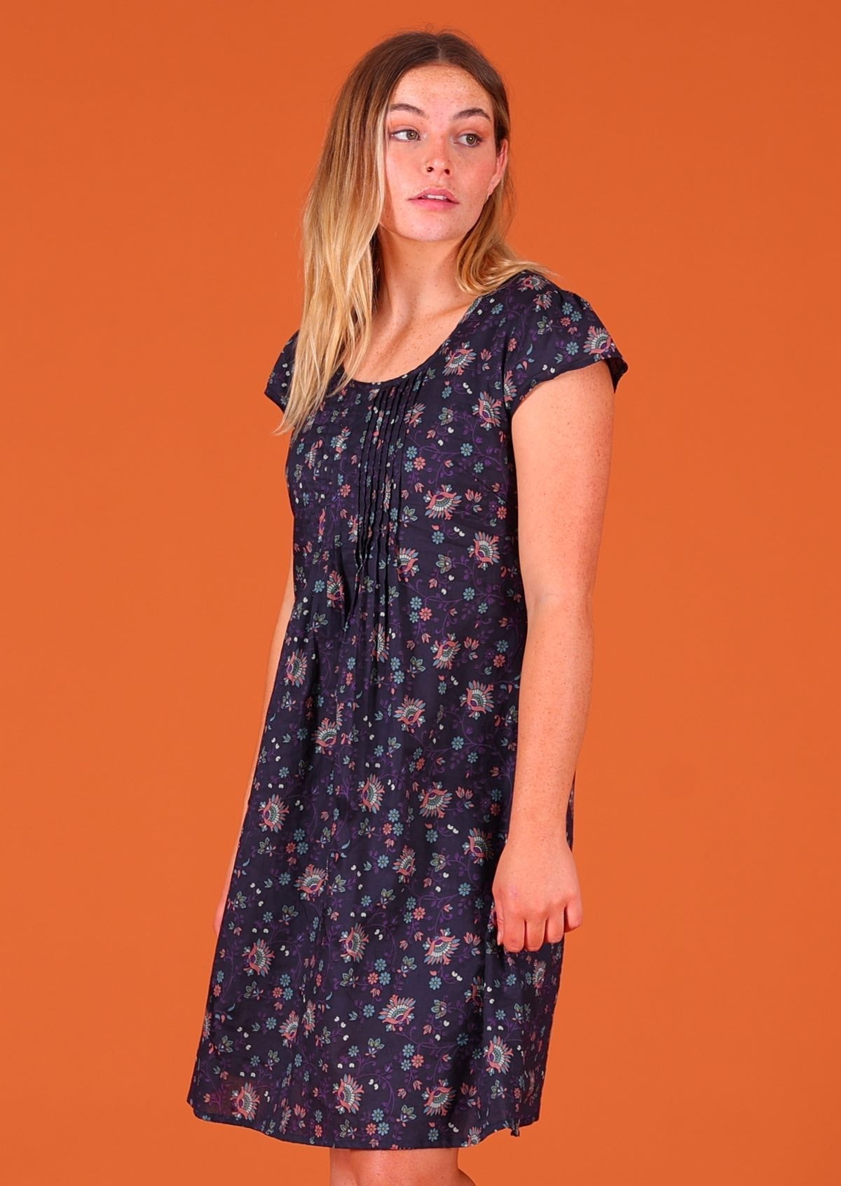 Model standing facing to the side wearing 100 percent cotton short sleeve pleated sundress in deep purple Indian floral