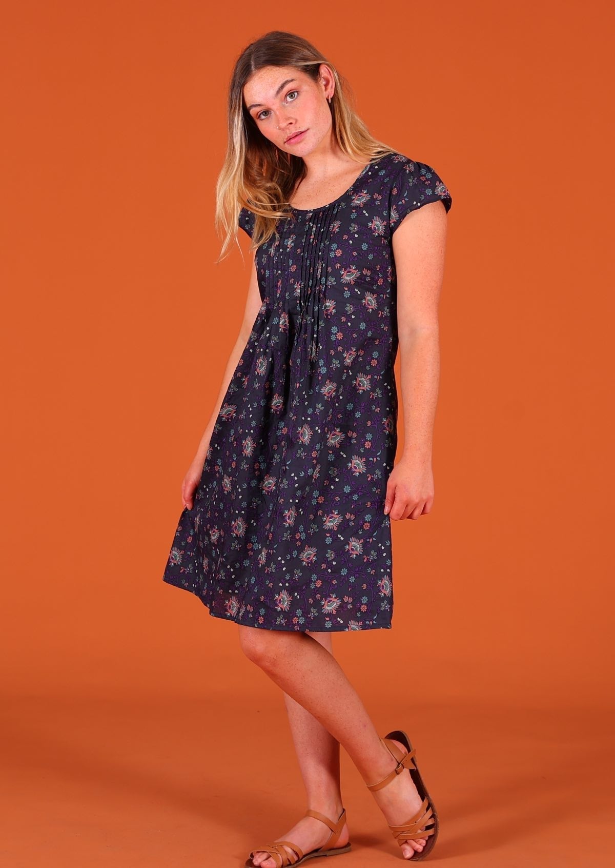 Model standing side on wearing 100 percent cotton short sleeve pleated sundress in deep purple Indian floral