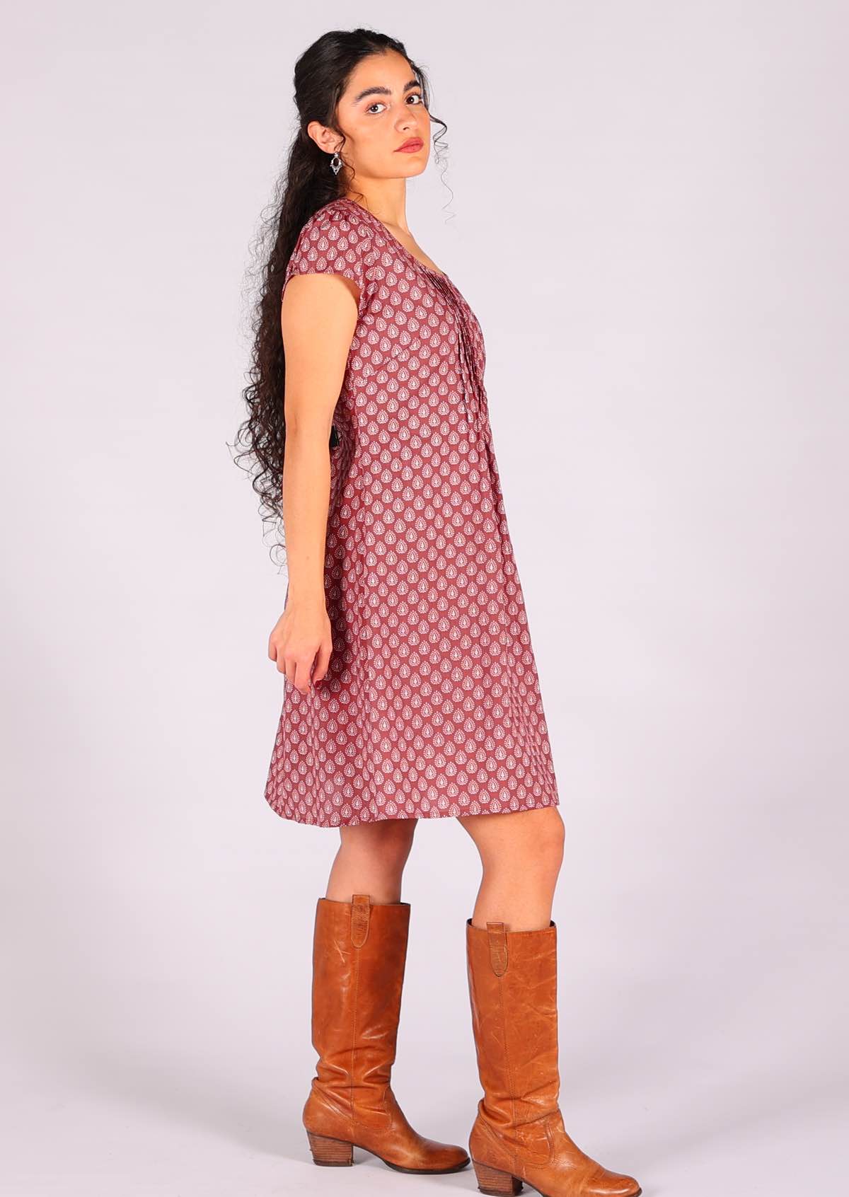 Model standing side on wearing 100 percent cotton short sleeve pleated sundress in dark terracotta