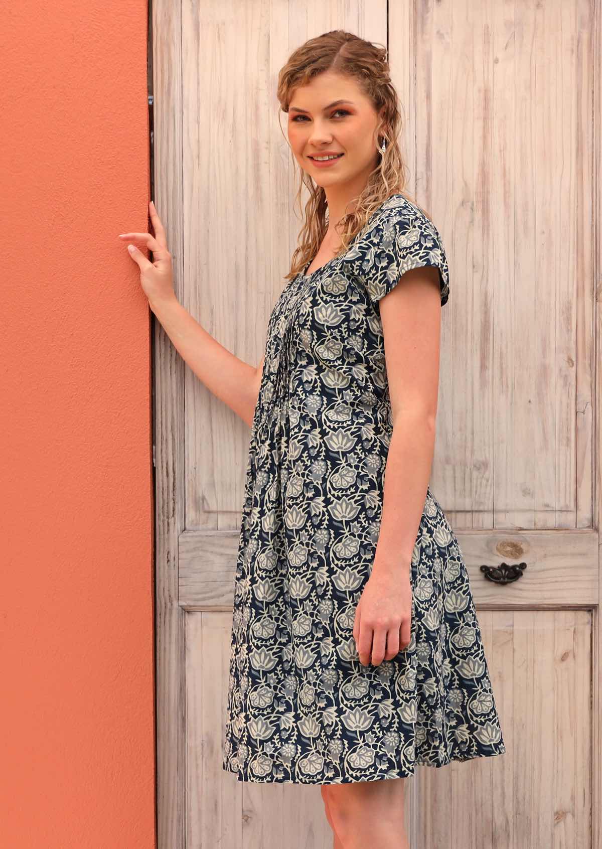 Smiling model stands on the side to showcase the fitted bodice and flowing skirt of the dress. 