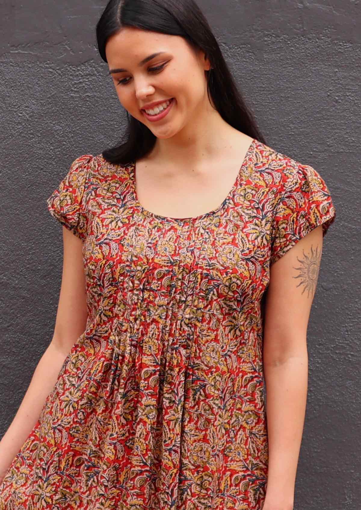 Woman with dark hair in  Indian print cotton sundress, close up of neck detail- lots of pin tucks under scoop neckline 