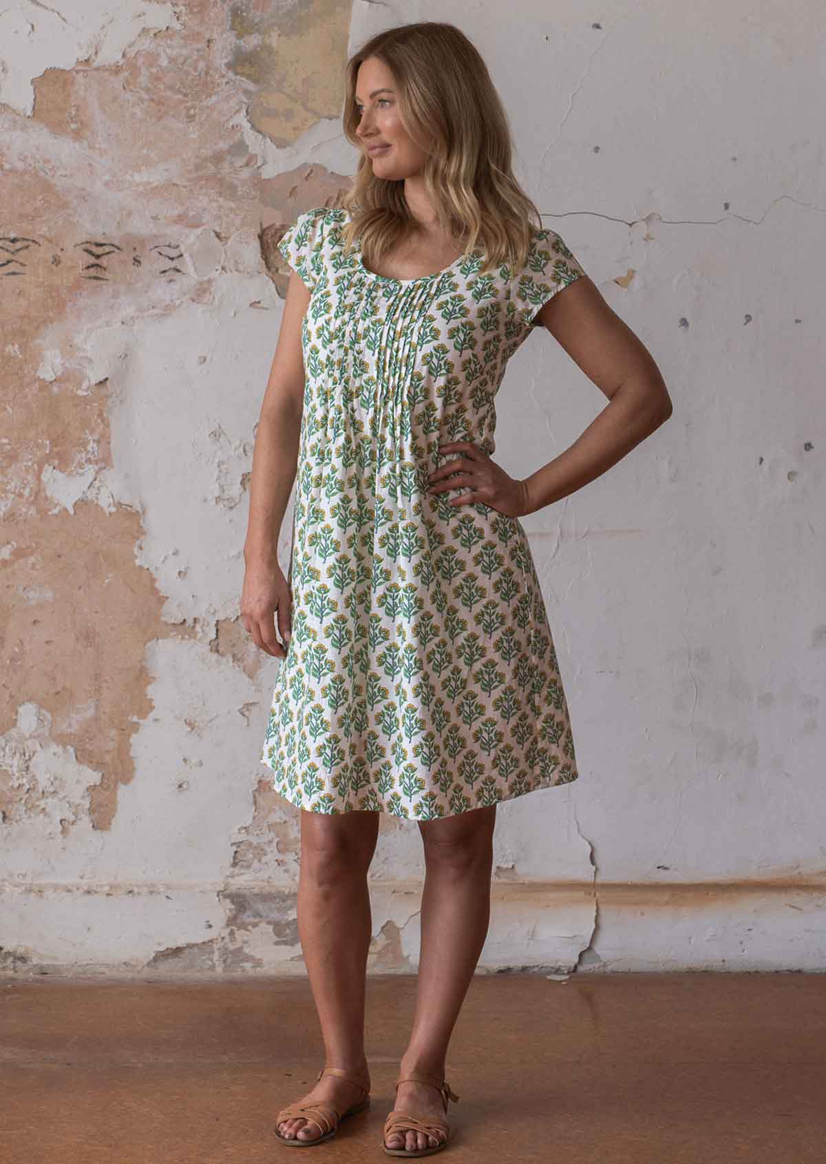 Woman poses in cotton cap sleeved above knee dress with yellow and green floral print on a white base