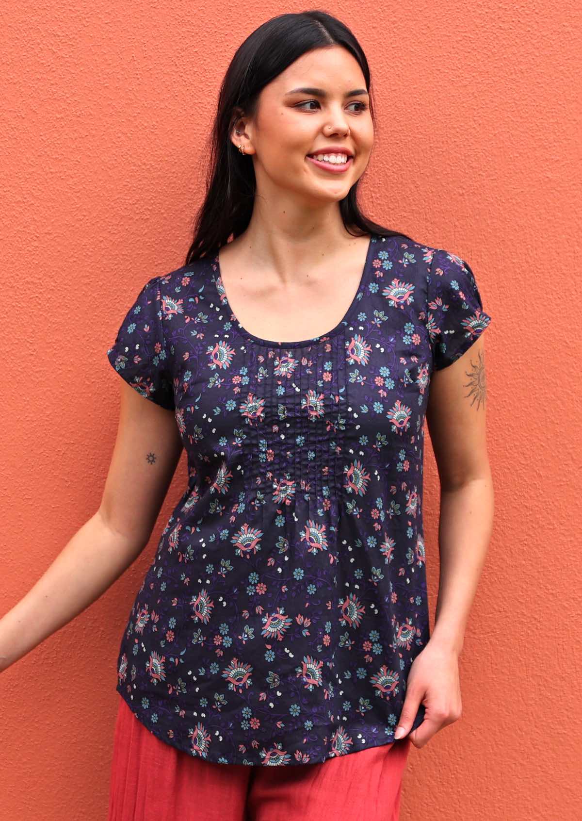 Model wears 100% cotton cap sleeve top with floral print in pink, teal and purple on a dark base