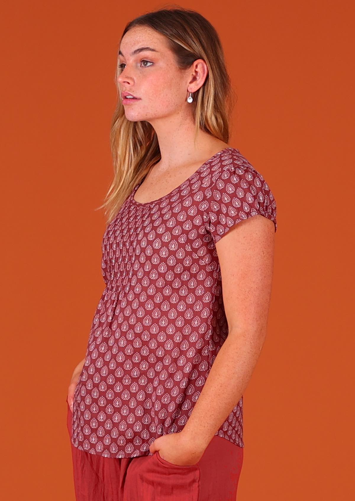 Model standing and facing to the side wearing 100 percent cotton Indian block print short sleeve pleated blouse dark terracotta