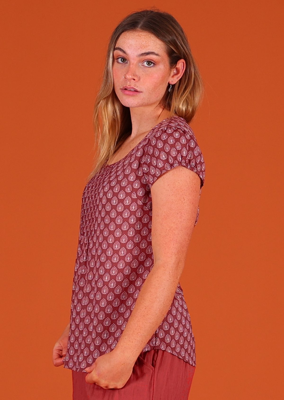 Model standing sideways wearing 100 percent cotton Indian block print short sleeve pleated blouse dark terracotta