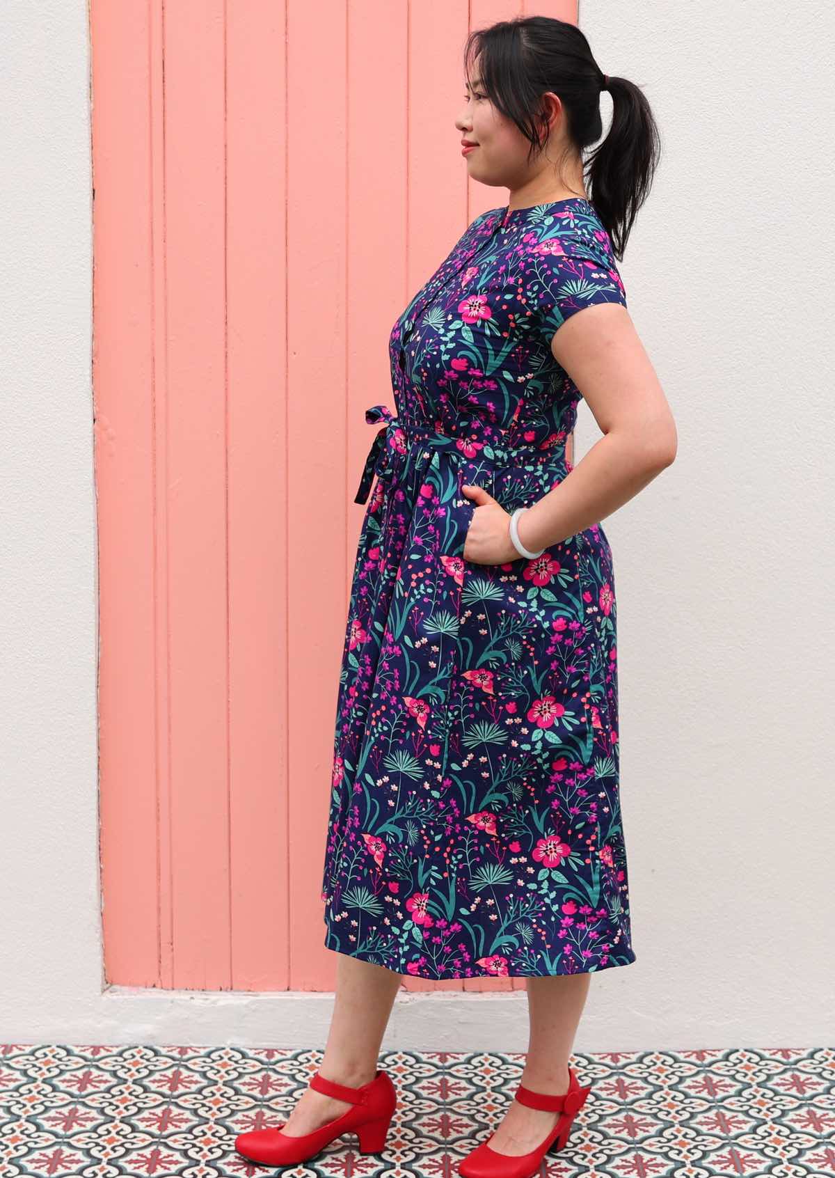 Woman standing in Navy cotton floral maxi dress with belt and hands in pockets 