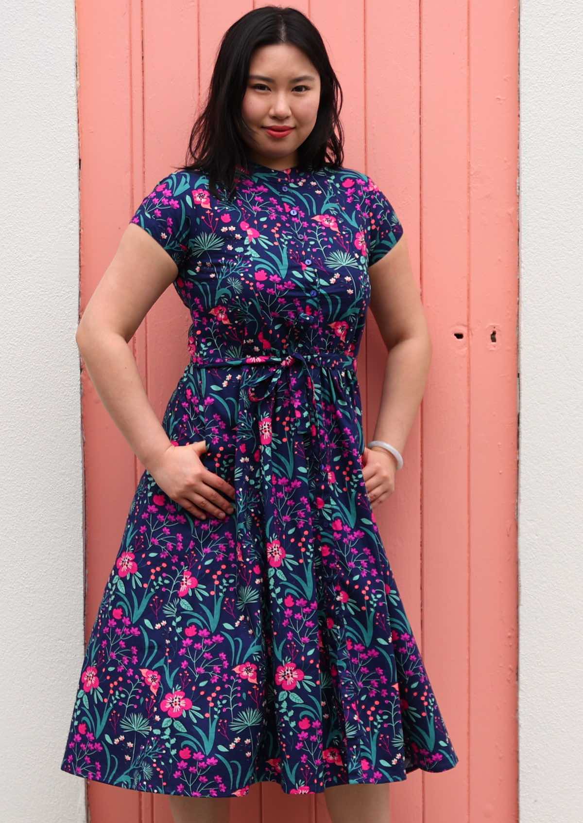 Woman standing in Navy cotton floral maxi dress with mandarin collar and hand in pockets 