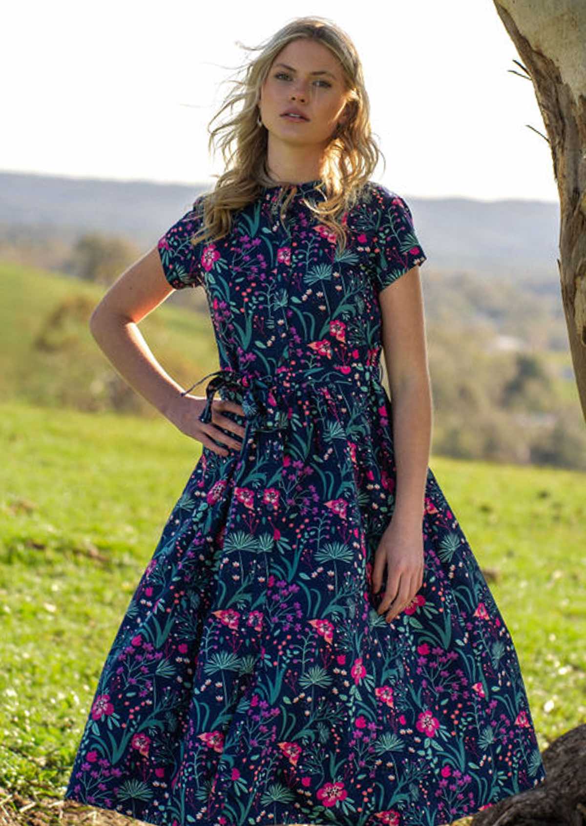 Woman standing under in Navy cotton floral maxi dress with v-neck and hand in pockets 