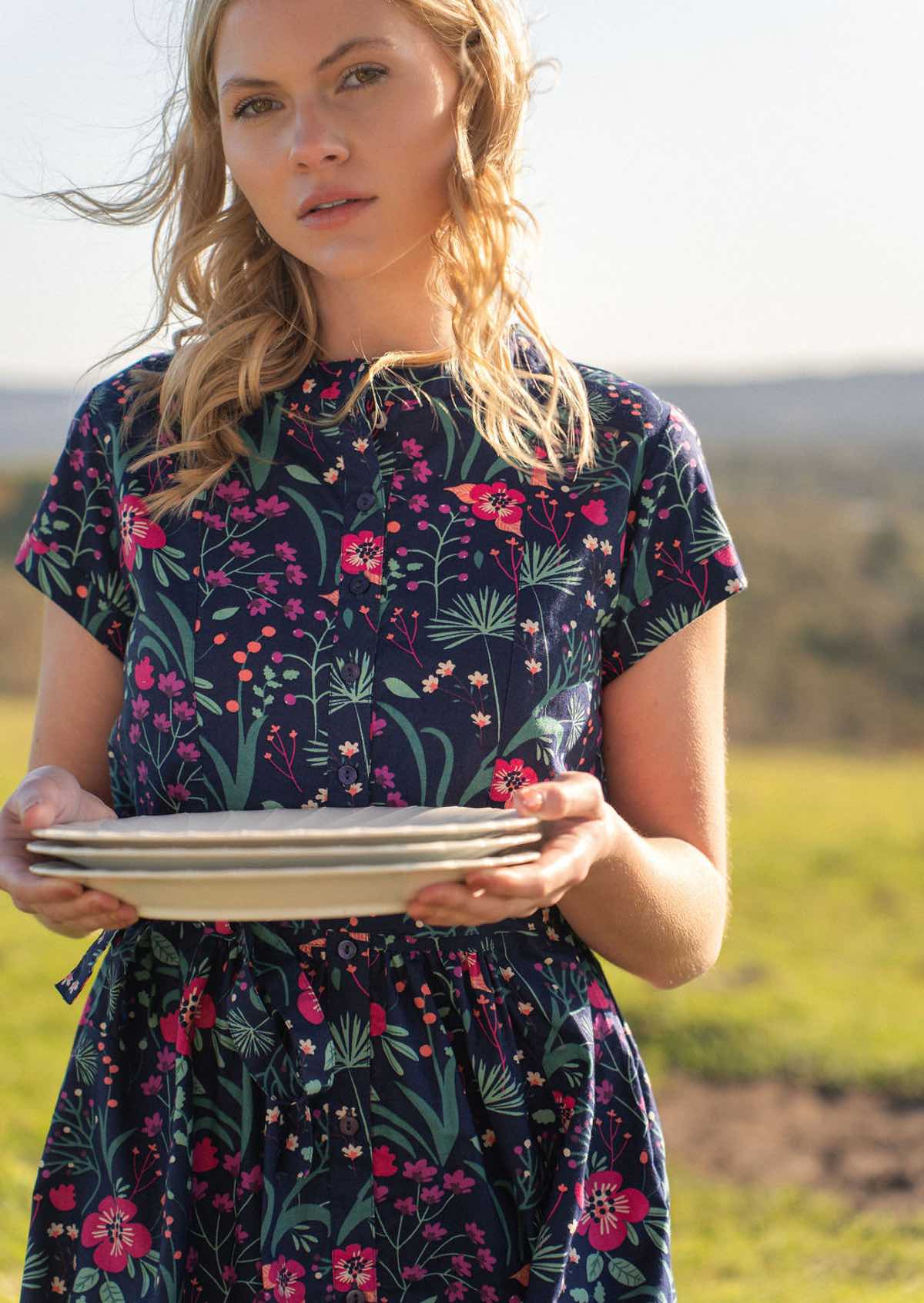 woman in navy cotton dress holding stack of plates