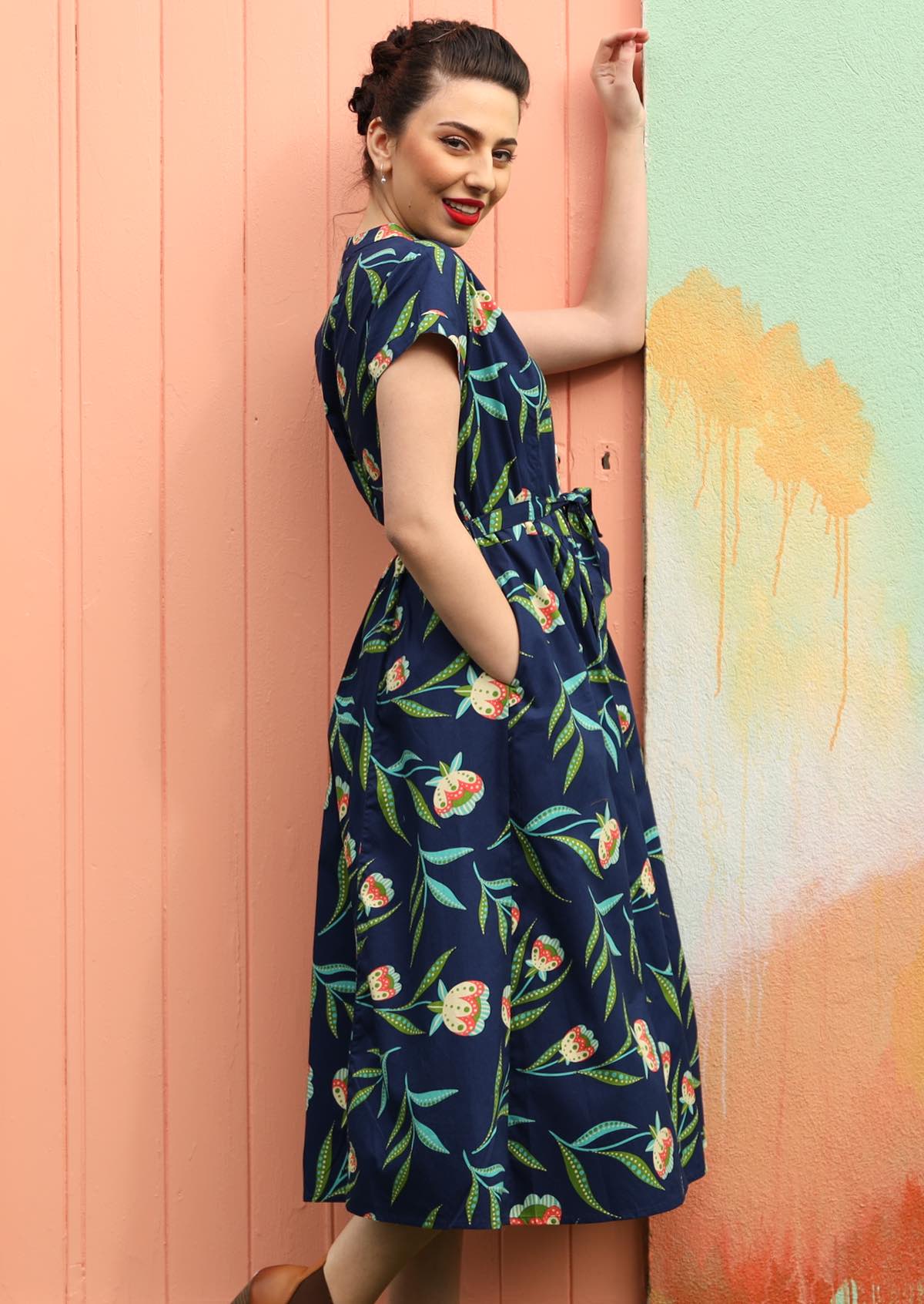 Model wears a navy blue dress with a floral pattern. 