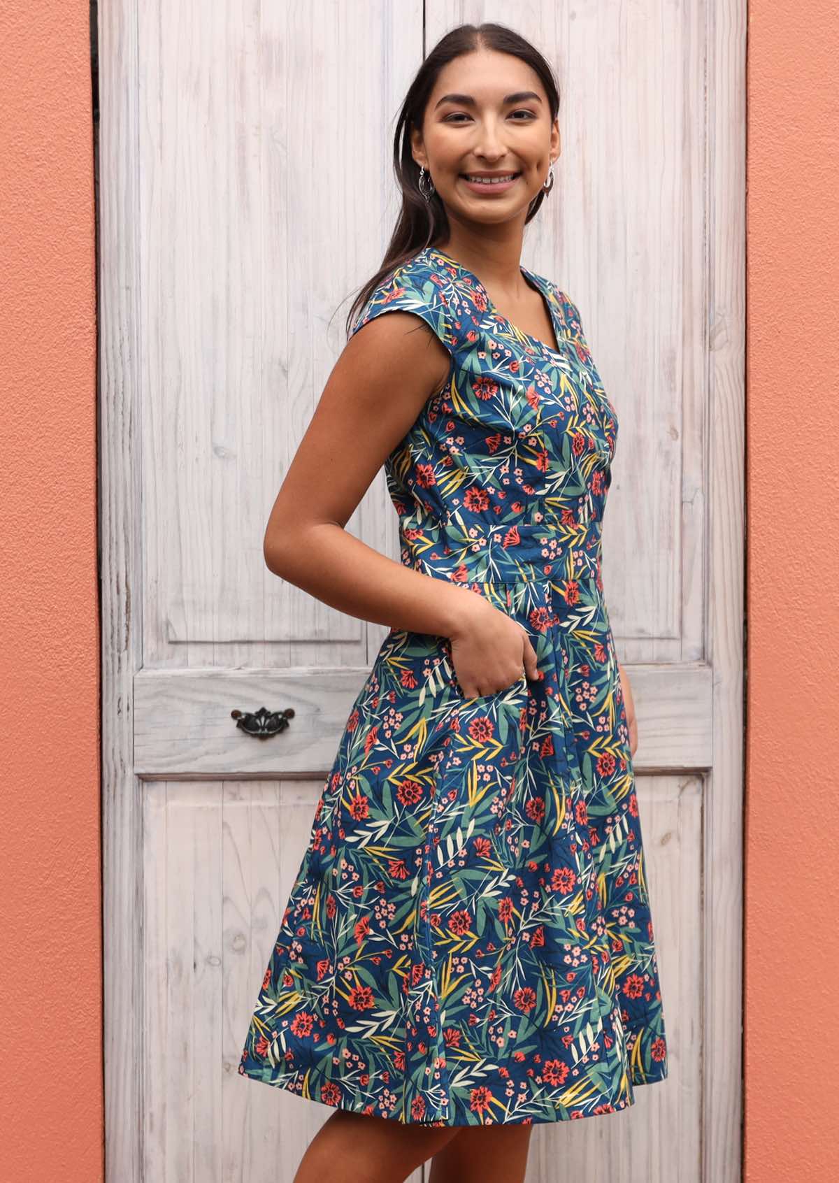 Smiling model has hands in the pockets of her retro style dress.