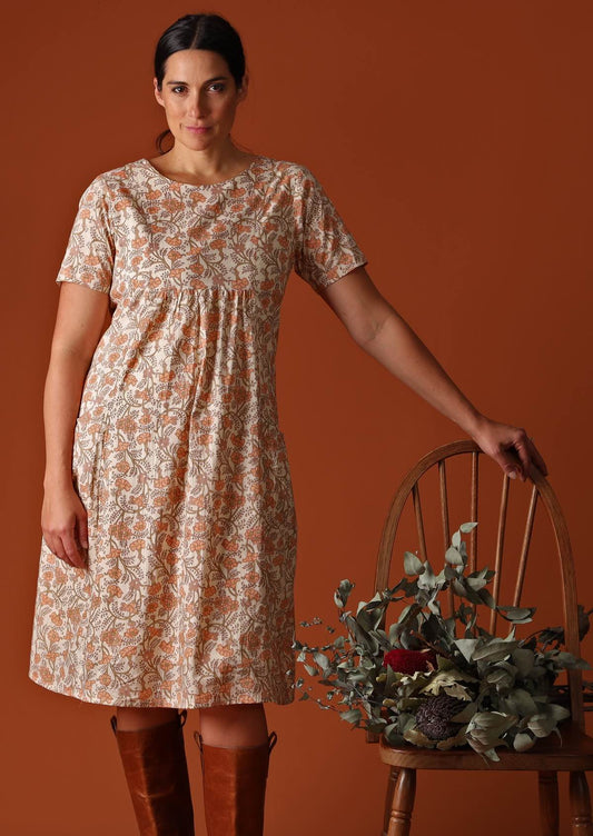 Model wears a 100% lightweight cotton knee length dress with pockets. The floral pattern of peach and olive green is on a cream base. This short sleeve dress is loose fit and lined.