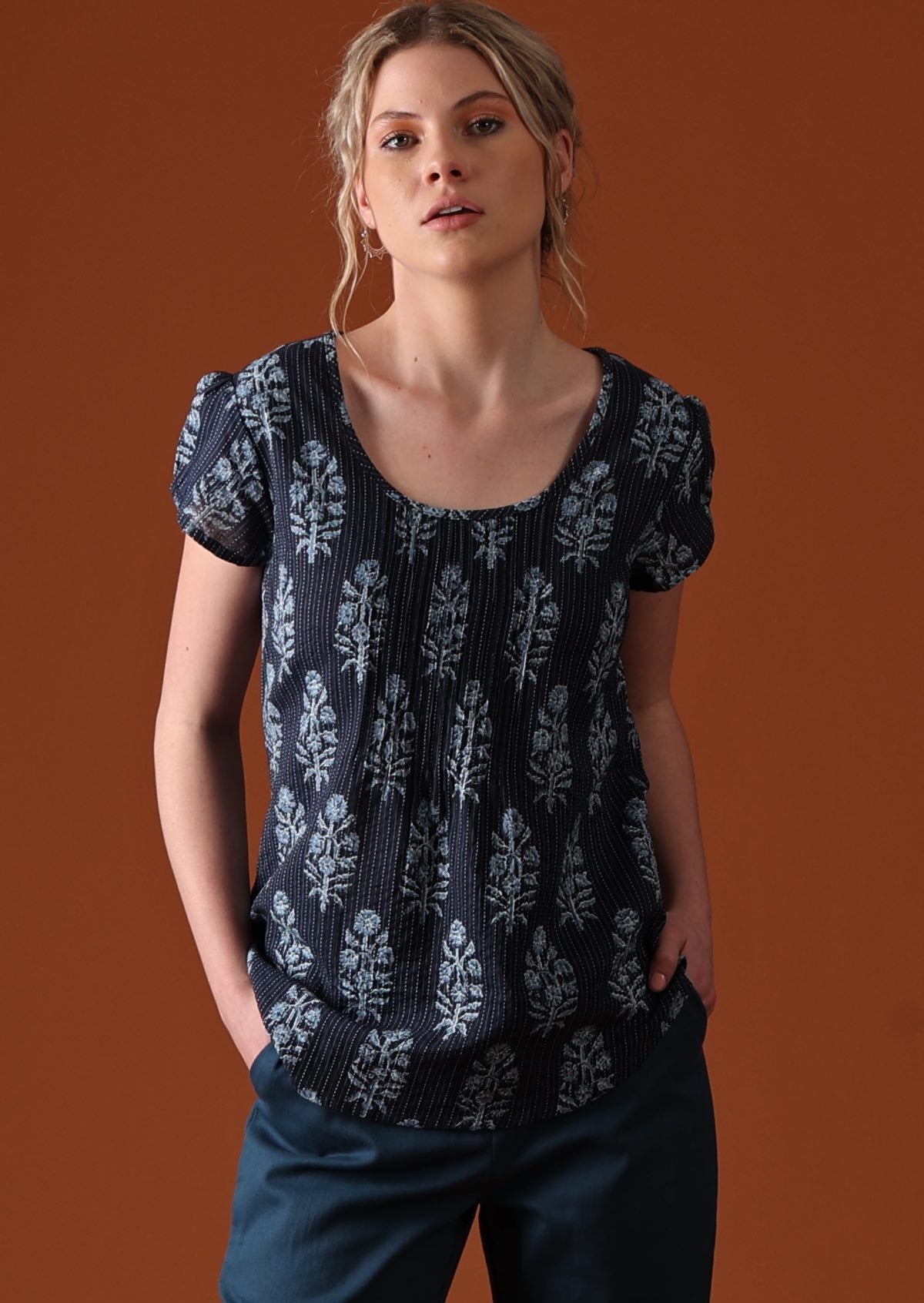 Model wears blue top with decorative pleats.